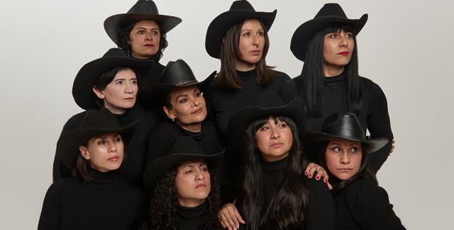 Nine women in black outfits and black cowboy hats pose like a family. They look as if they are seeing something off camera that makes them curious.