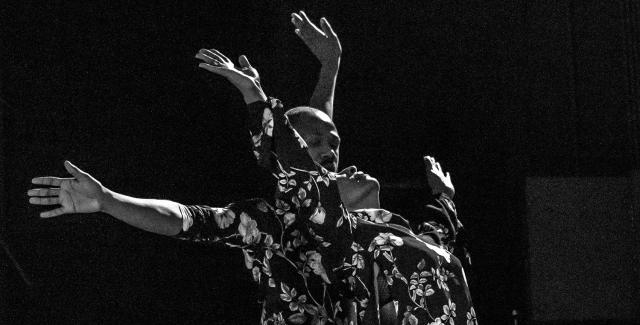 In black and white, two Black dancers perform in floral costumes.