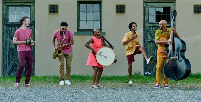 In front of an old ranch home, five musicians play and dance.