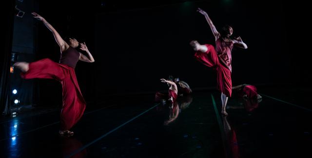 Three dancers, in red outfits, leap.