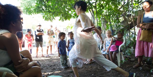 Outside and surrounded by a crowd of kids and adults, a woman leans on her front legs and throws her arms back.