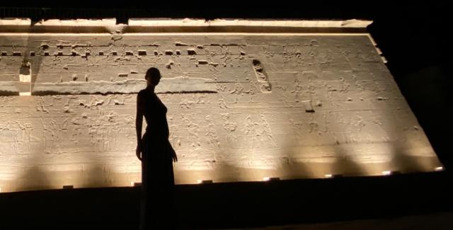 Silhouette of a woman, in front of a cream, stone wall that is underlit.