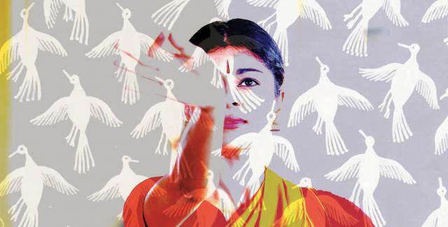 A woman in orange and yellow traditional Indian dress gestures with her hand at images of crows