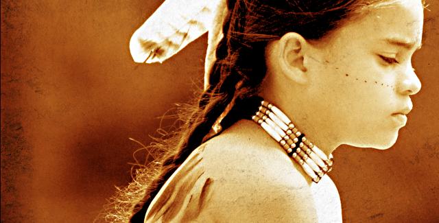A young boy wears a feather in her braid, a beaded choker, and body paint.