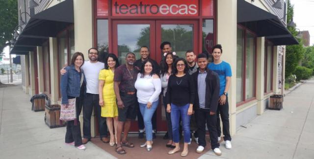 Twelve members of Teatro ECAS stand together on the sidewalk outside of the theater