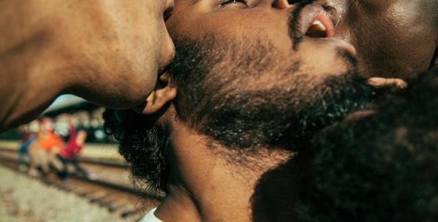 Three men are in very close proximity with their mouths agape against each other