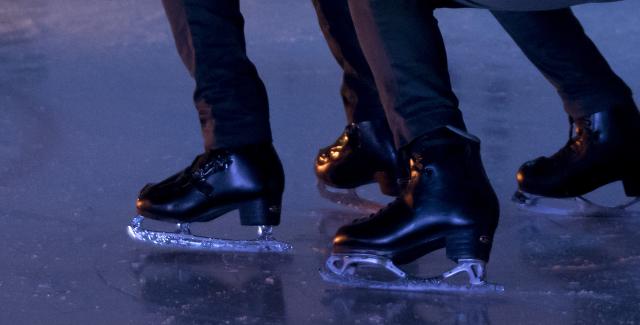 A Black ice skater leans over the back of another Black ice skater.