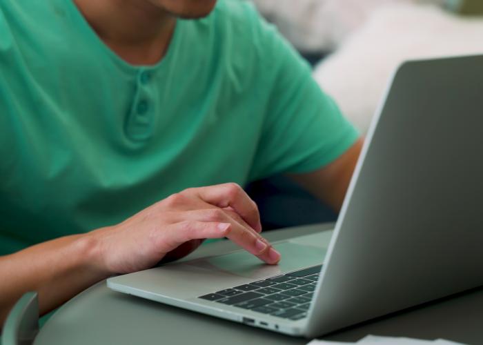 A brown man types on his laptop.
