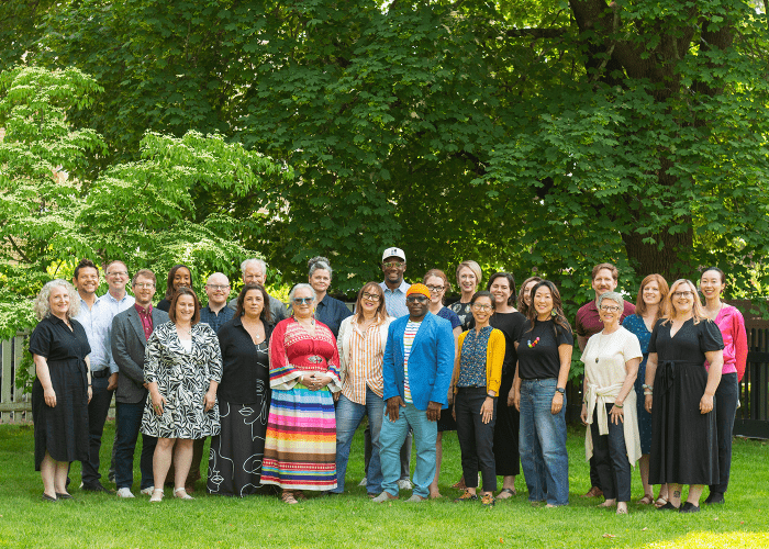 Outside, a large group of smiling folks in a mix of muted and vibrant outfits.