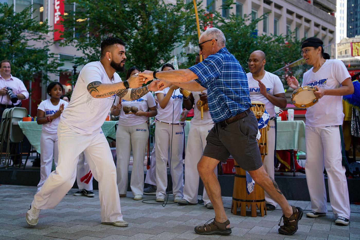 A Brown man holds the hands of an elderly white man while they dance.