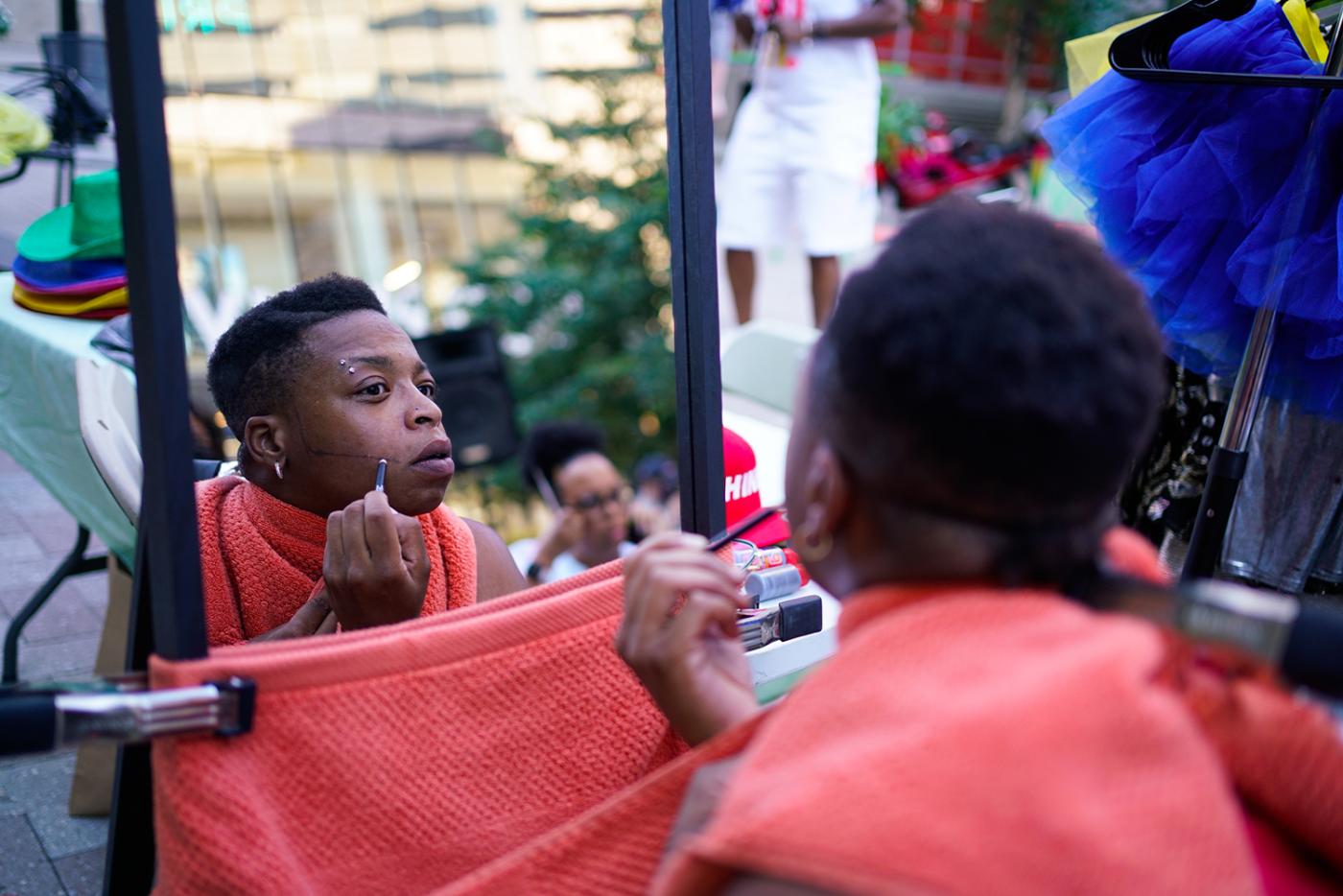 A Black person applies makeup in a mirror.