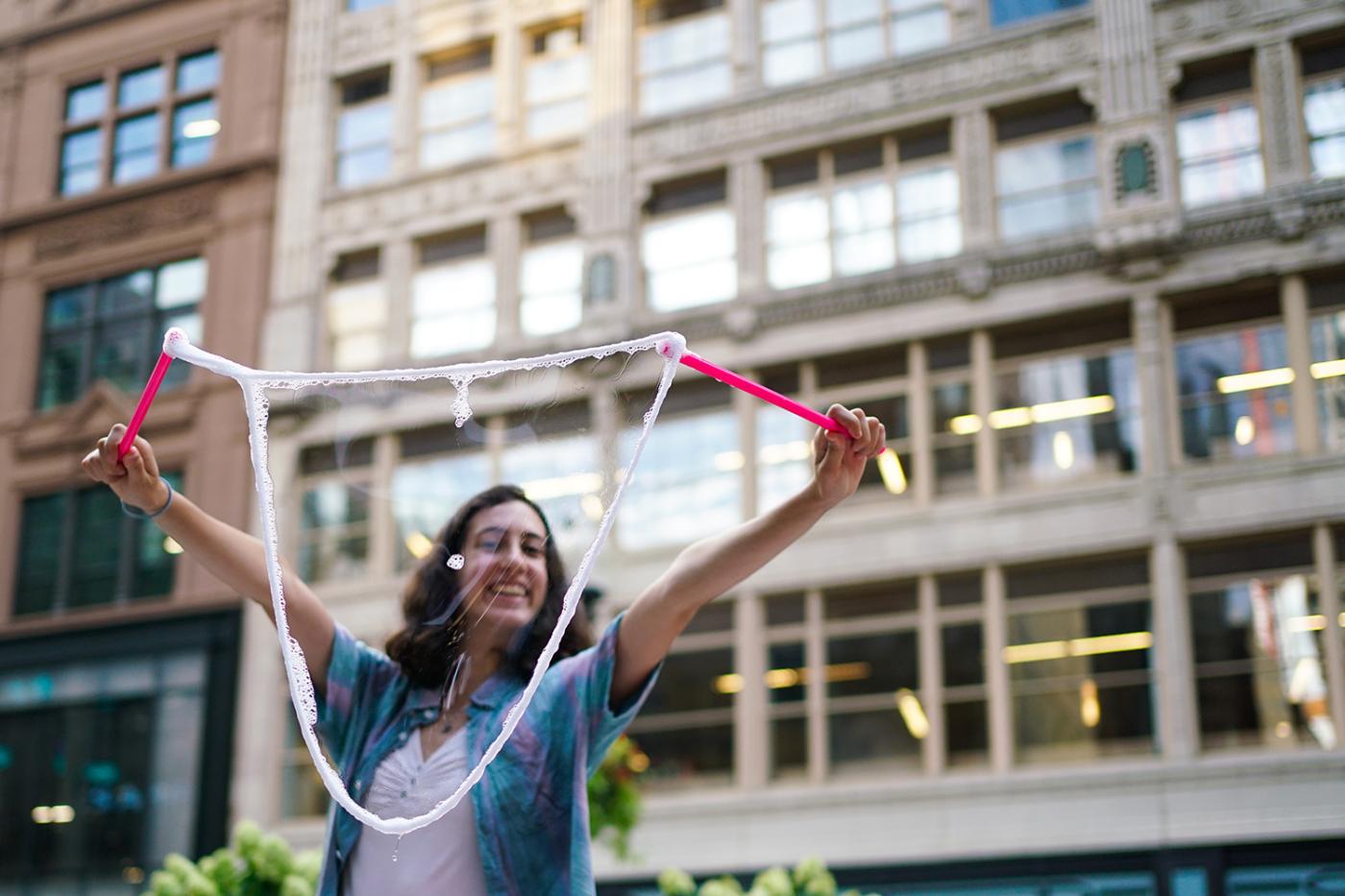 A white lady uses a bubble wand to create a huge bubble.