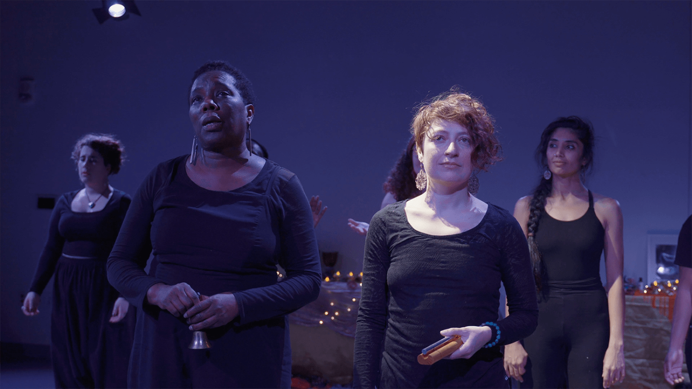 On a stage, in black outfits, black, brown, and white women smile and look around.