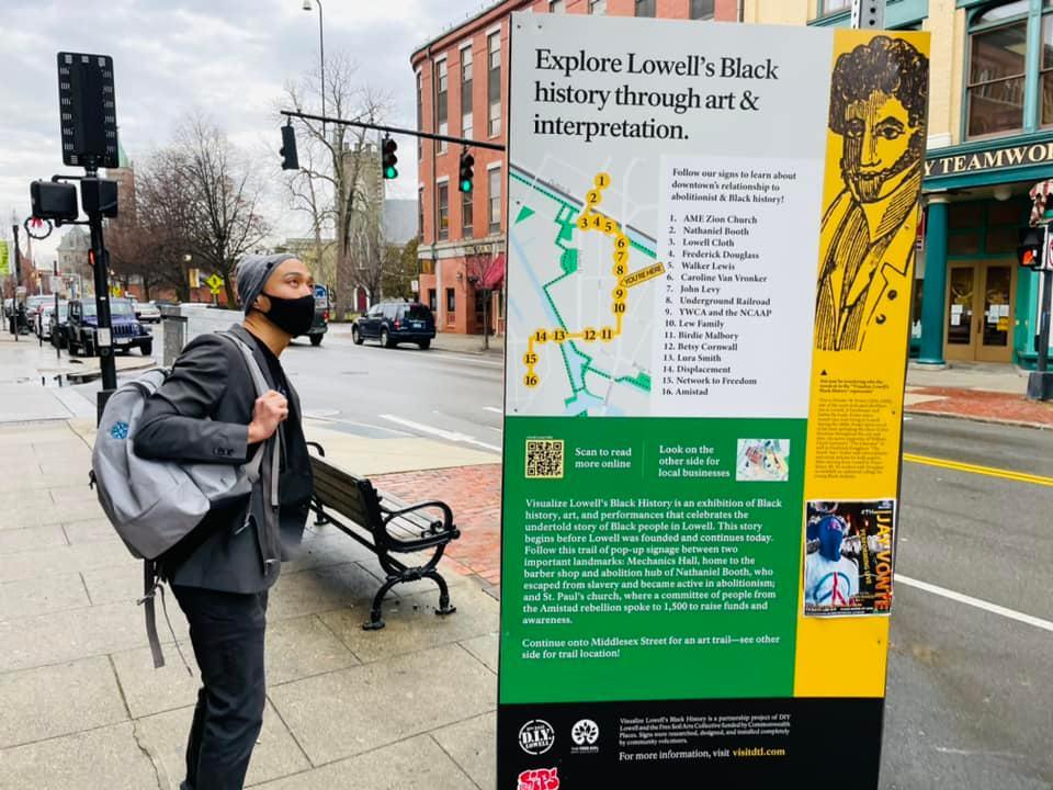 A person, in a face mask, looks at a map of Black historical locations and artwork in Lowell.