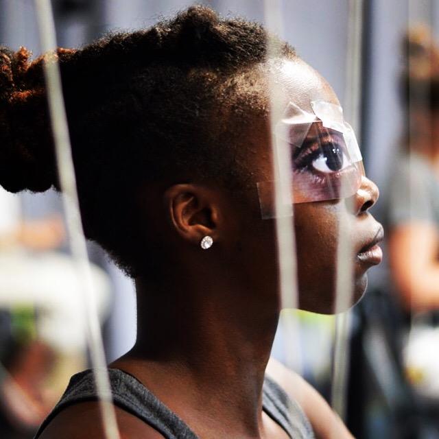 A young black girl wears a mask taped over her eyes of bigger eyes.