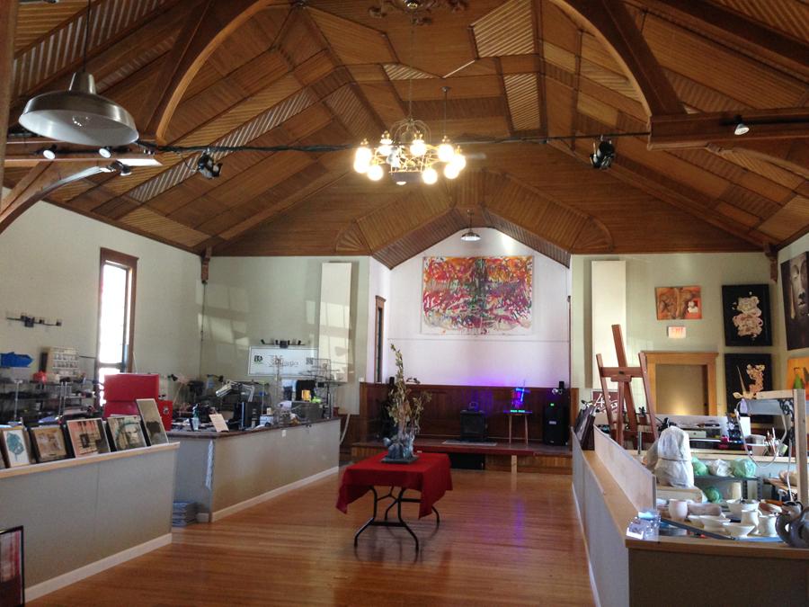 Interior of a high ceiling room within a converted church. Displays of local artists are on tables lining the walls