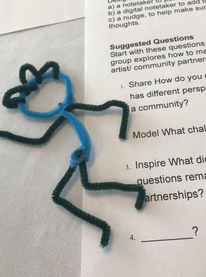 A figure made of pipe cleaners is on a table over an event worksheet.