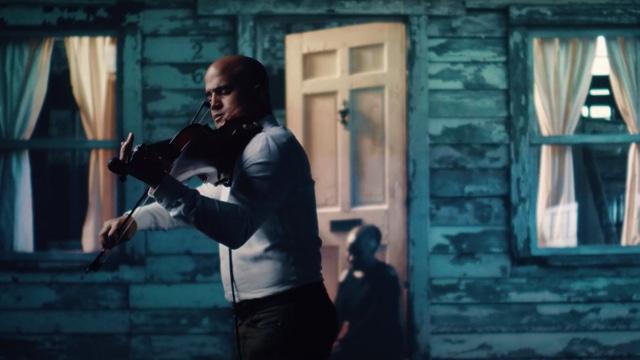 In front of a backdrop of the facade of a home, Daniel plays the violin.