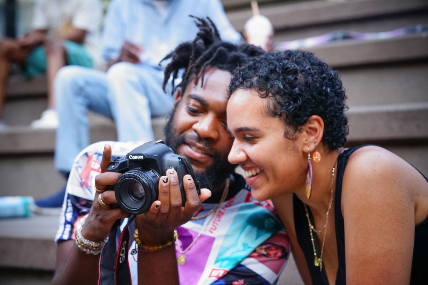 A Black man and woman look at the backside of a digital camera together and smile.