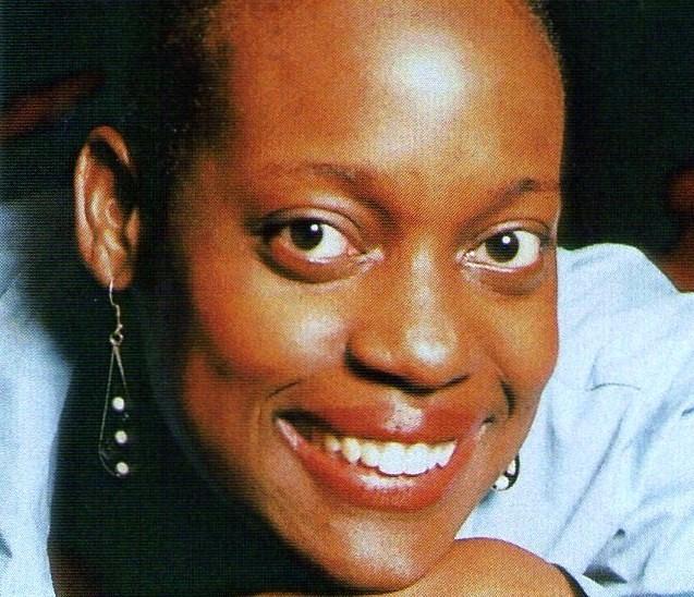 A smiling Black woman wearing a blue top and dangling earrings