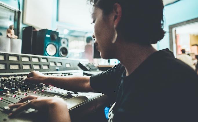 a person sits in a sound mixing booth adjusting various sliders