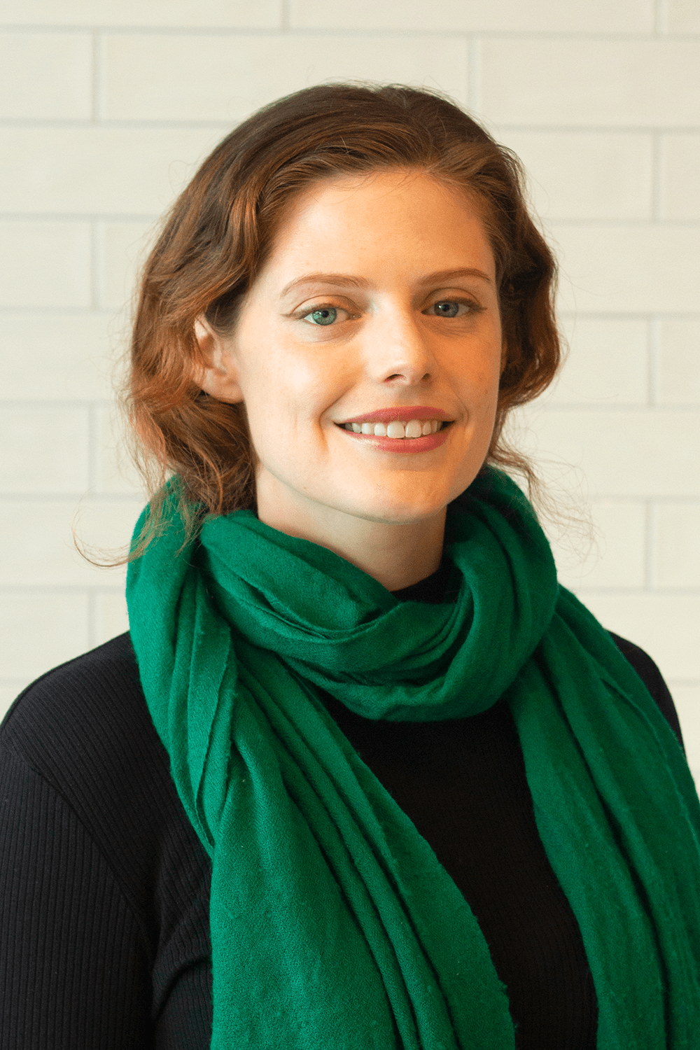 Emm has her auburn hair pulled back. She wears a green scarf that matches her eyes.