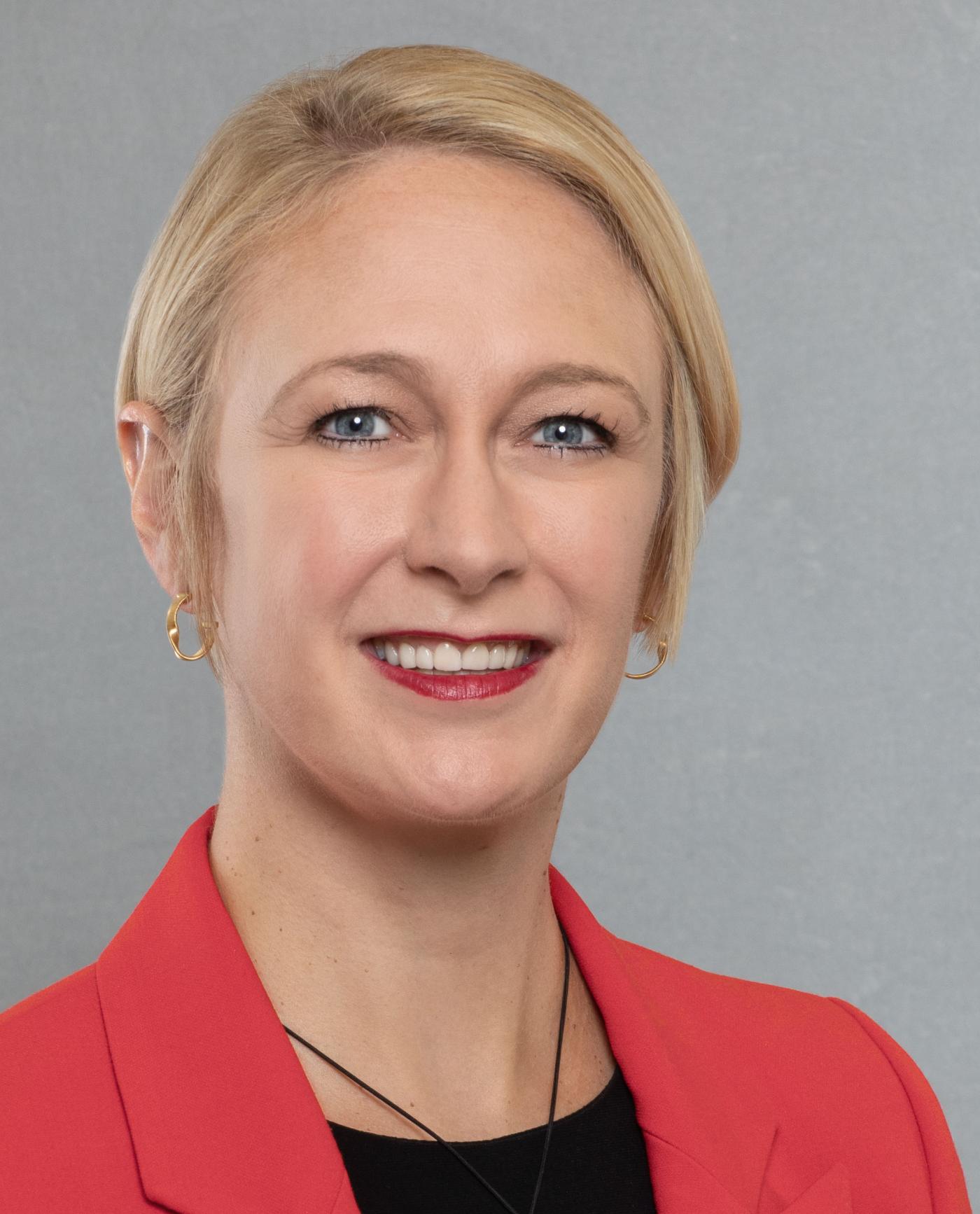 A woman with short blonde hair wearing a red blazer and black shirt.