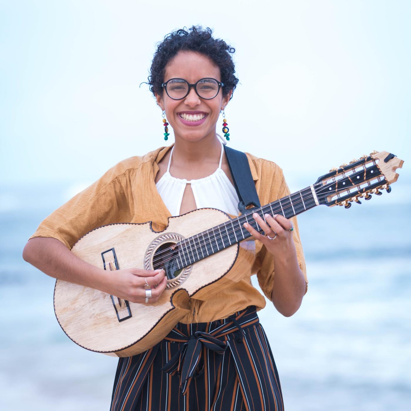 Fabiola plays the cuatro in front of the ocean.