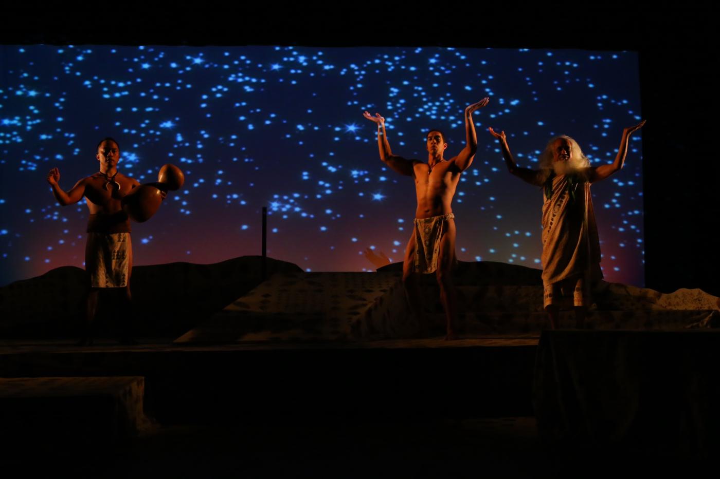 In front of a starry night backdrop, three men of different ages pose with their arms held up towards the sky.