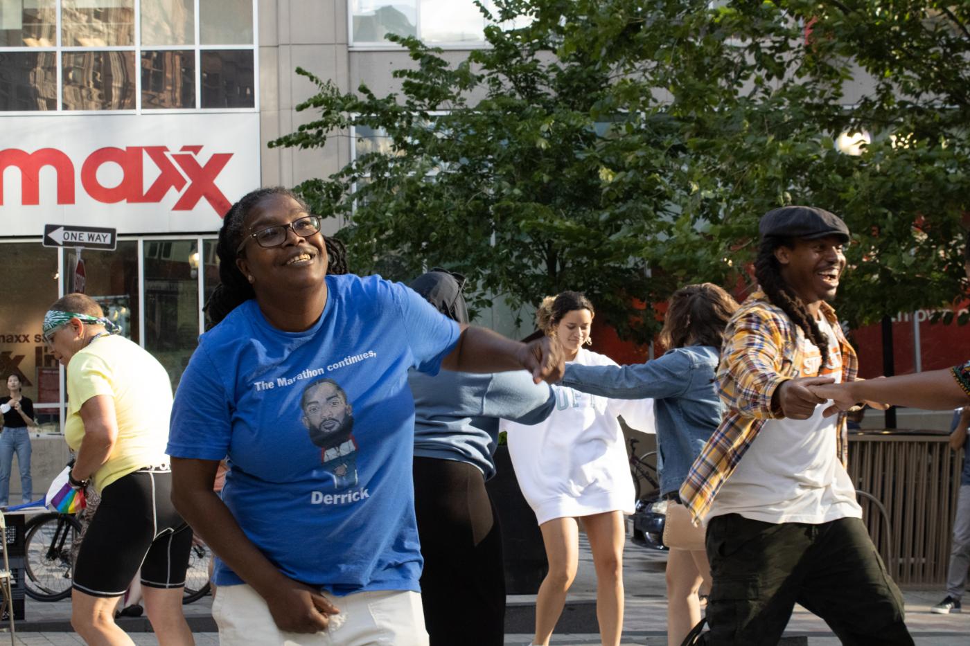 Outside, in a city center by stores, folks of color dance and smile.