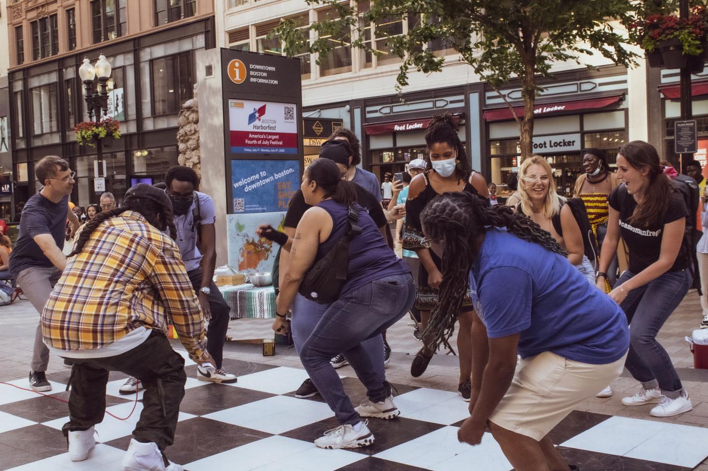 On a checkerboard ground, a group of folks of color dance. 