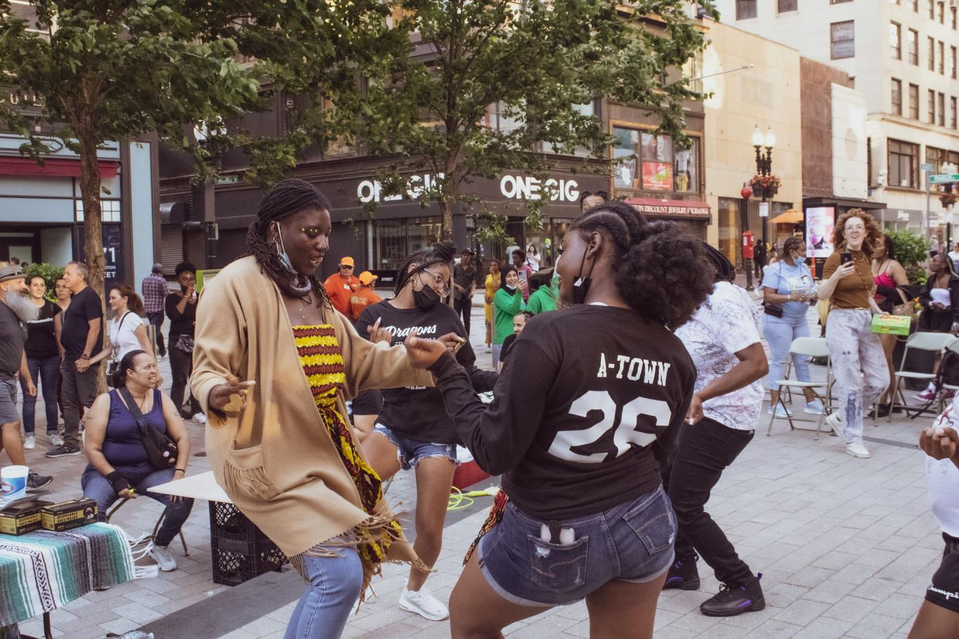 On a city street, four Black women dance together.