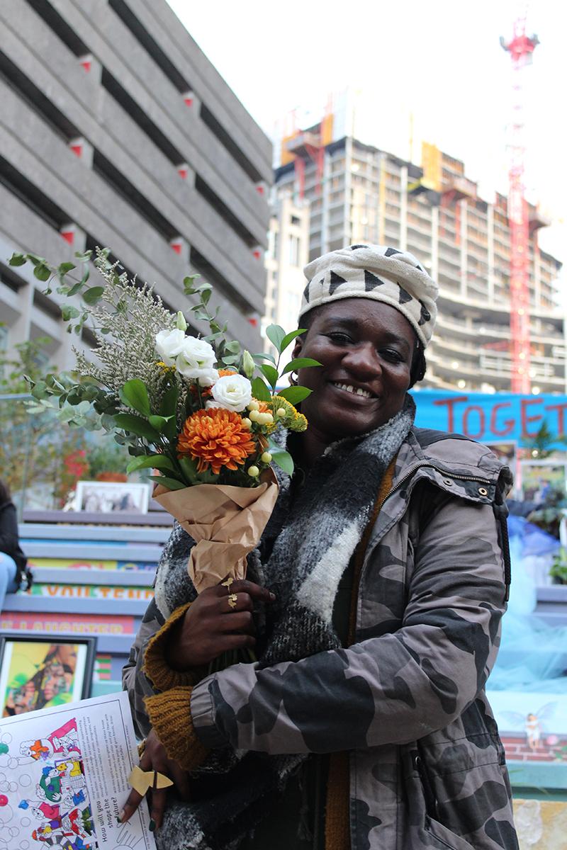 A Black woman holds a bouquet in front of steps with art work on it.
