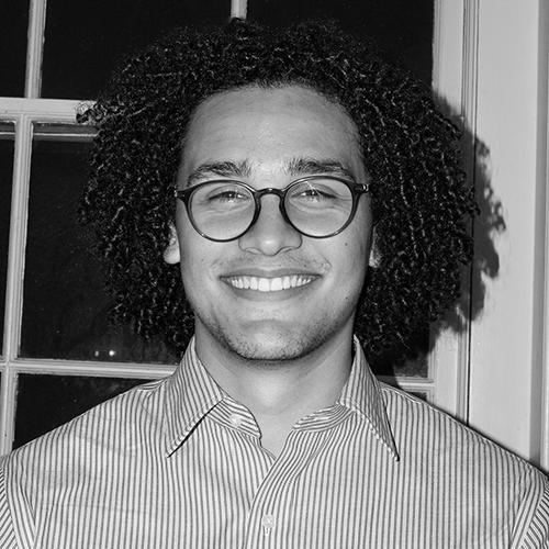 Jameson smiles. He has shoulder-length hair and wears round eyeglass frames.