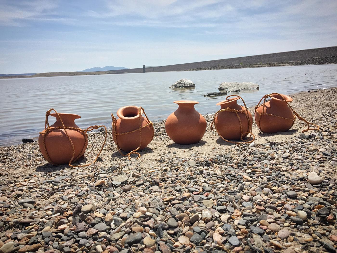 Ceramic water jugs, tied together with a rope, rest on a rocky beach.