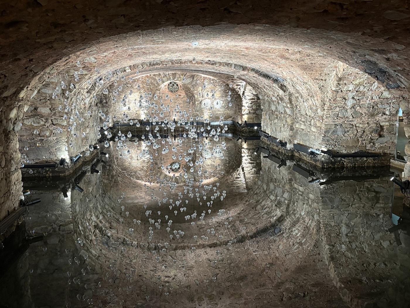 In a room with an arched ceiling, metal "droplets" hang creating the illusion of rain.