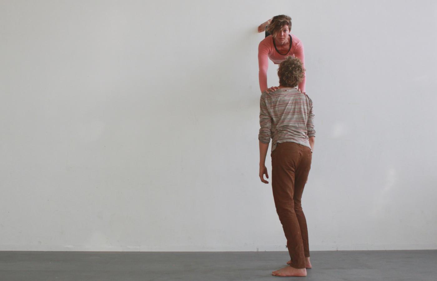 A white woman dances on a wall while leaning on a white man.