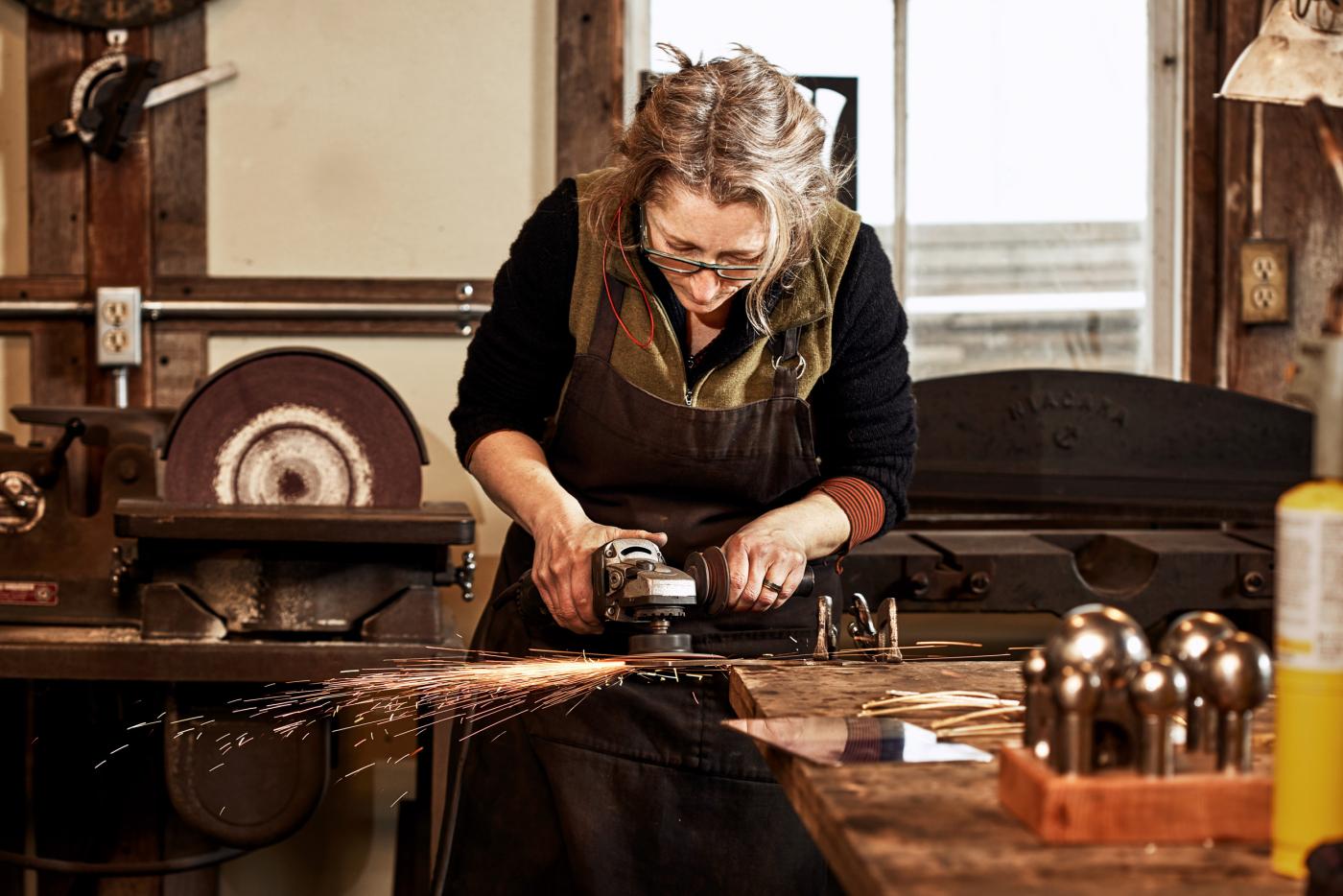 Maine Crafts Association image of Erica Moody, metal smith, making sparks fly in her studio.