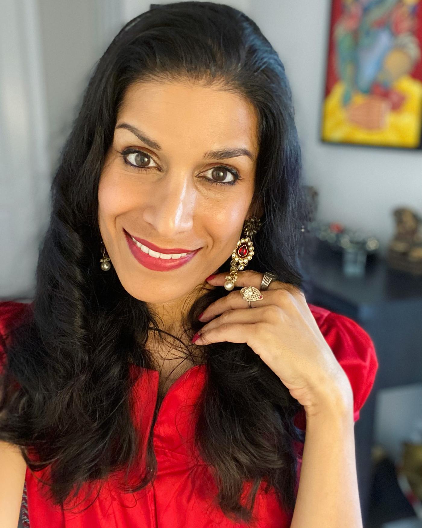 Mesma is an Indian woman with red lips, a red ruby earring, and a bright red shirt. 