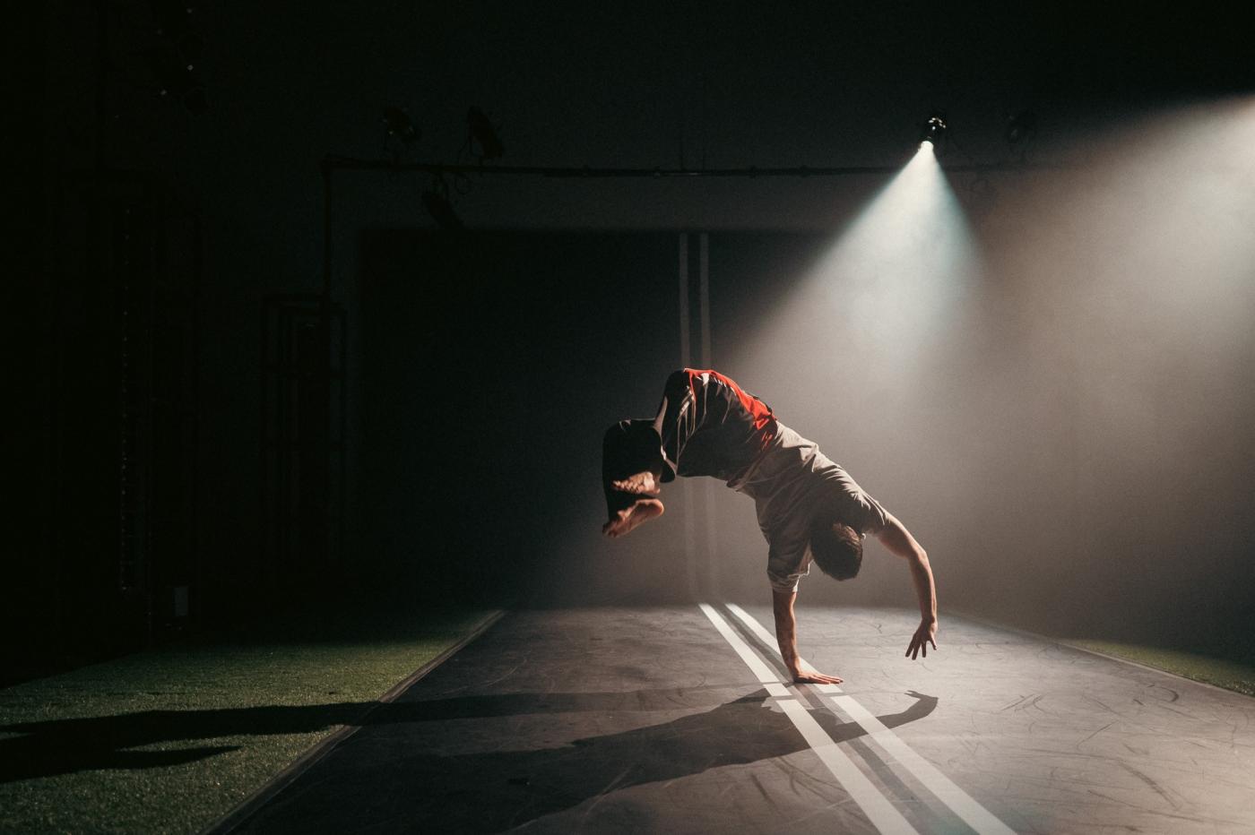In a spotlight and on a road that appears to continue up the wall, a dancer does a flip.