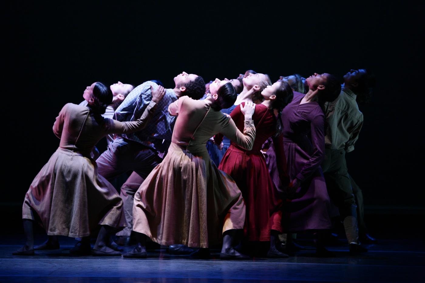 On a dark stage, a group of folks lean back and look up at the overhead spotlight.