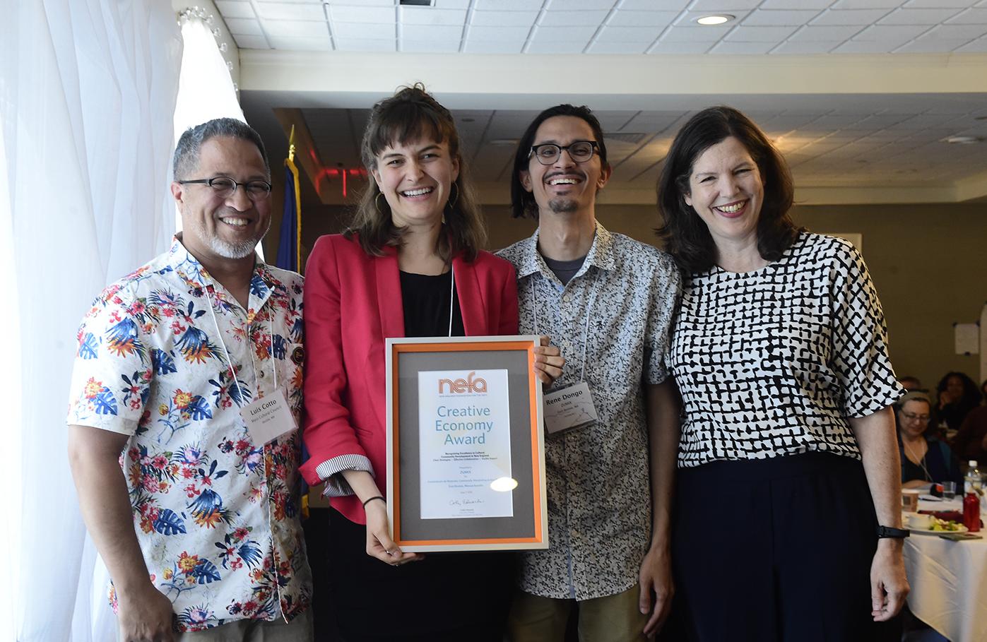 4 people stand shoulder to shoulder; one holds framed award that reads NEFA's Creative Economy Award