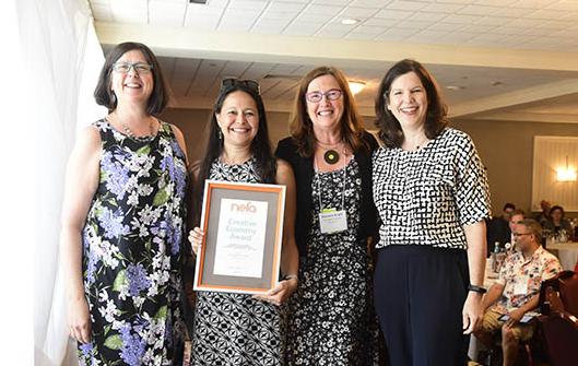 4 people stand shoulder to shoulder; one holds framed award that reads NEFA's Creative Economy Award