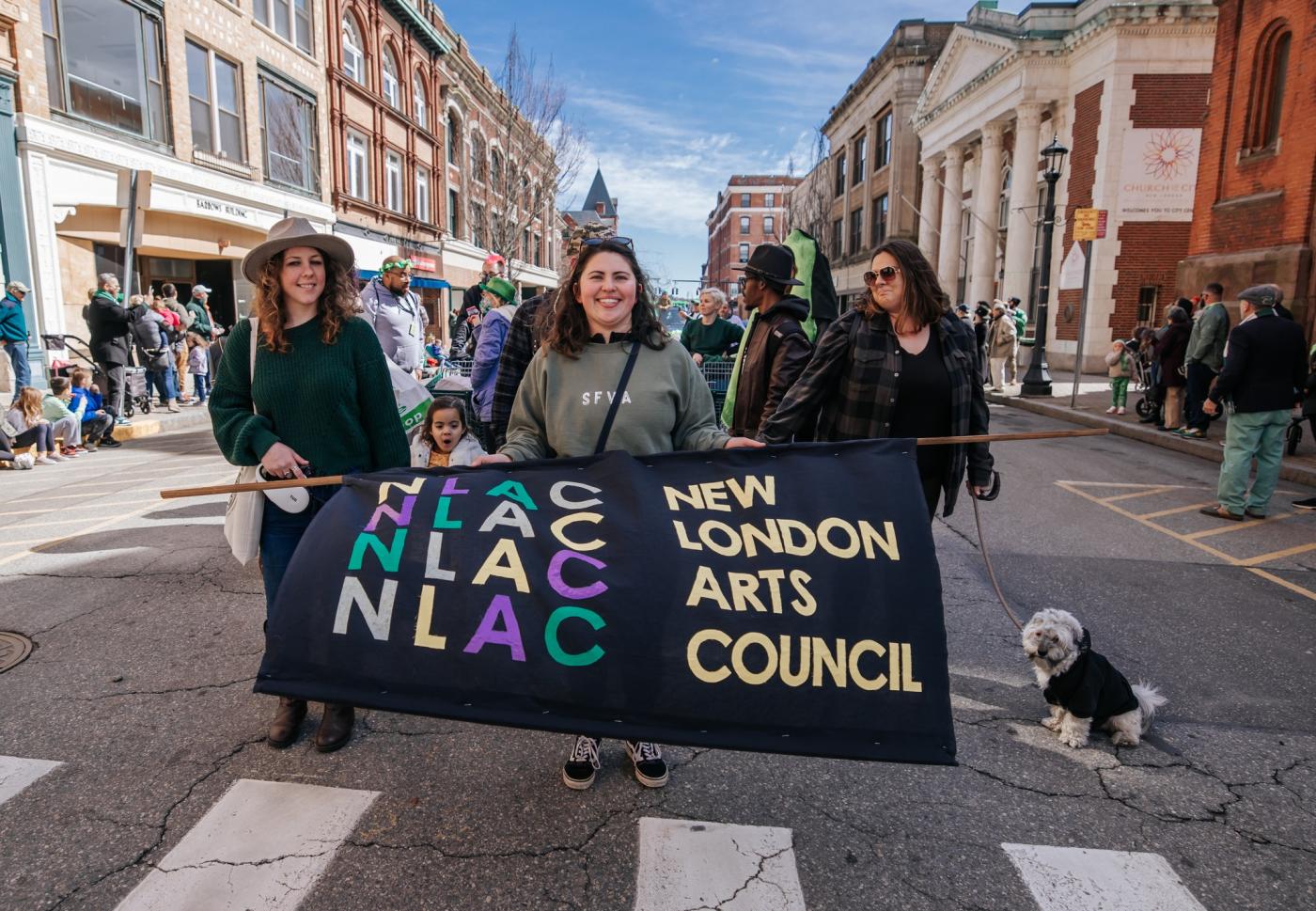Three girls and a dog pose behind a banner that reads "New London Arts Council."