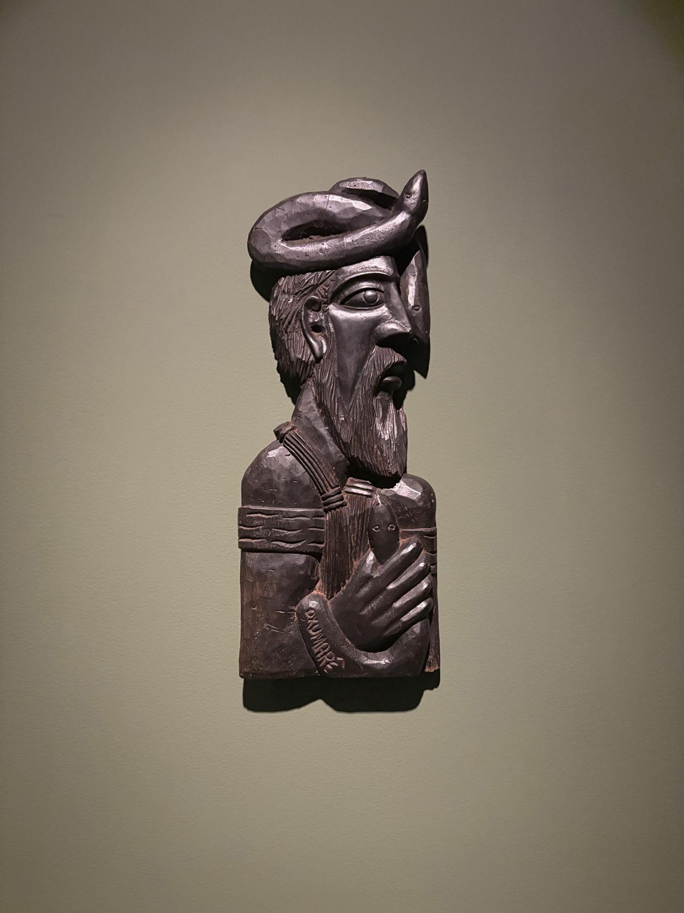 On a wall, a wood sculpture of a man in a round hat with a beard.