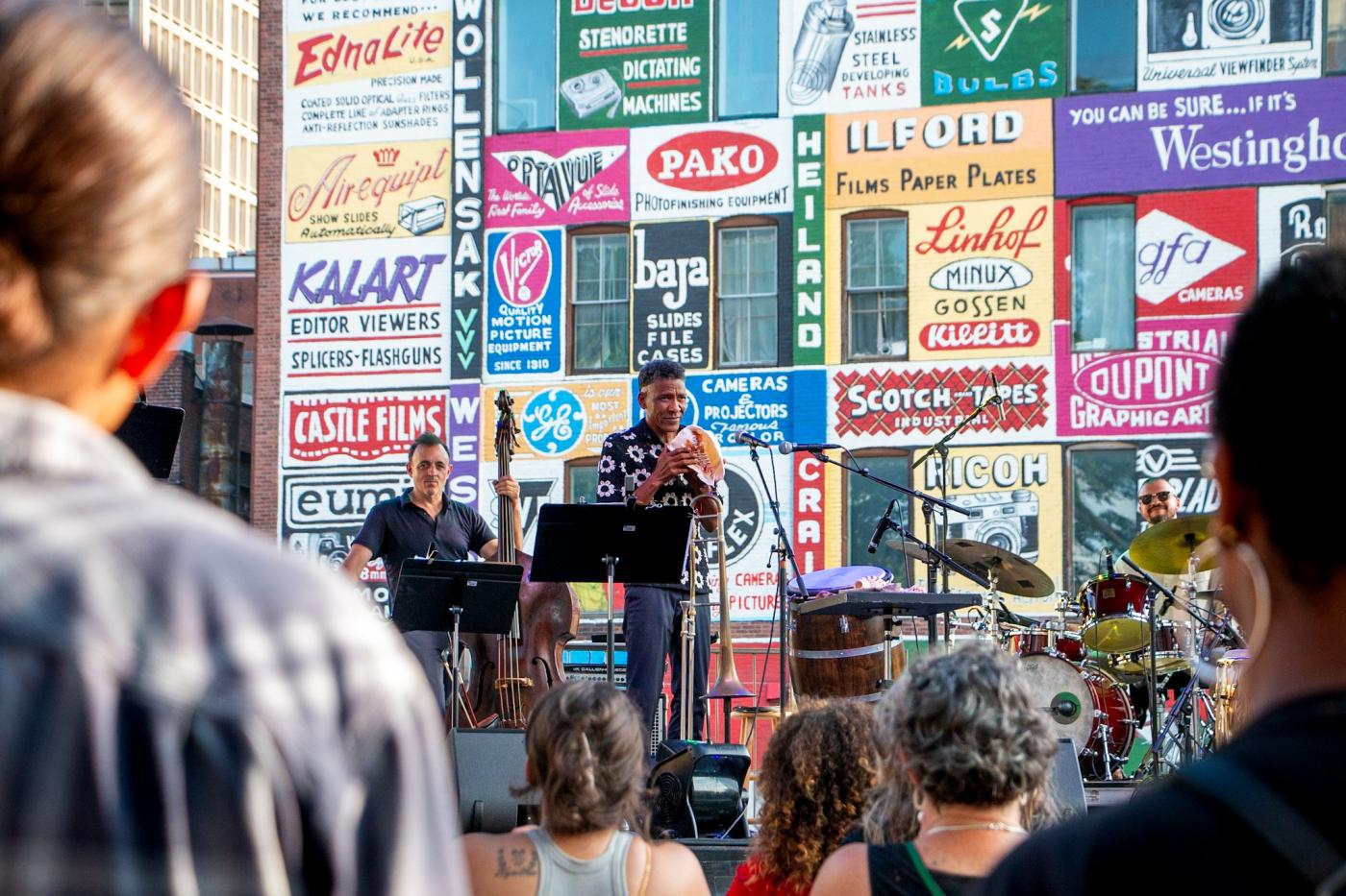A crowd watches a man play the conch shell and two other members of his band.