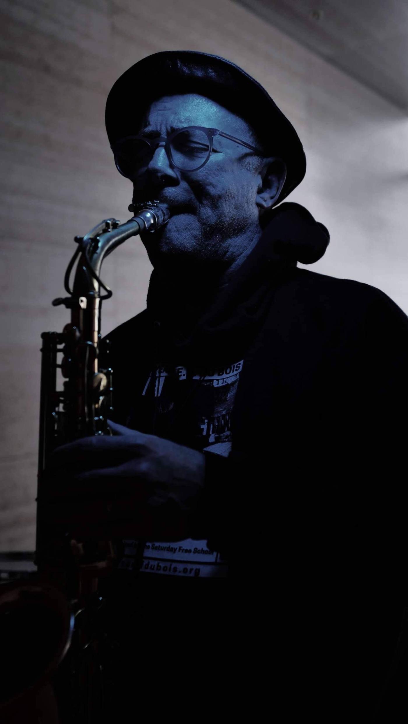 A white man, in a top hat, plays the saxopone.