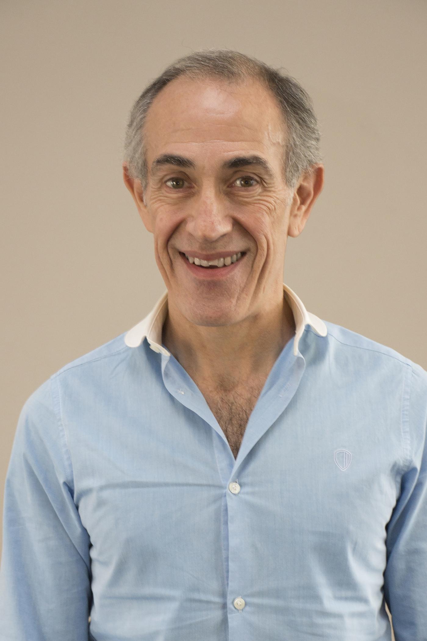 A man with short gray hair and wearing a blue button down shirt with a white collar.