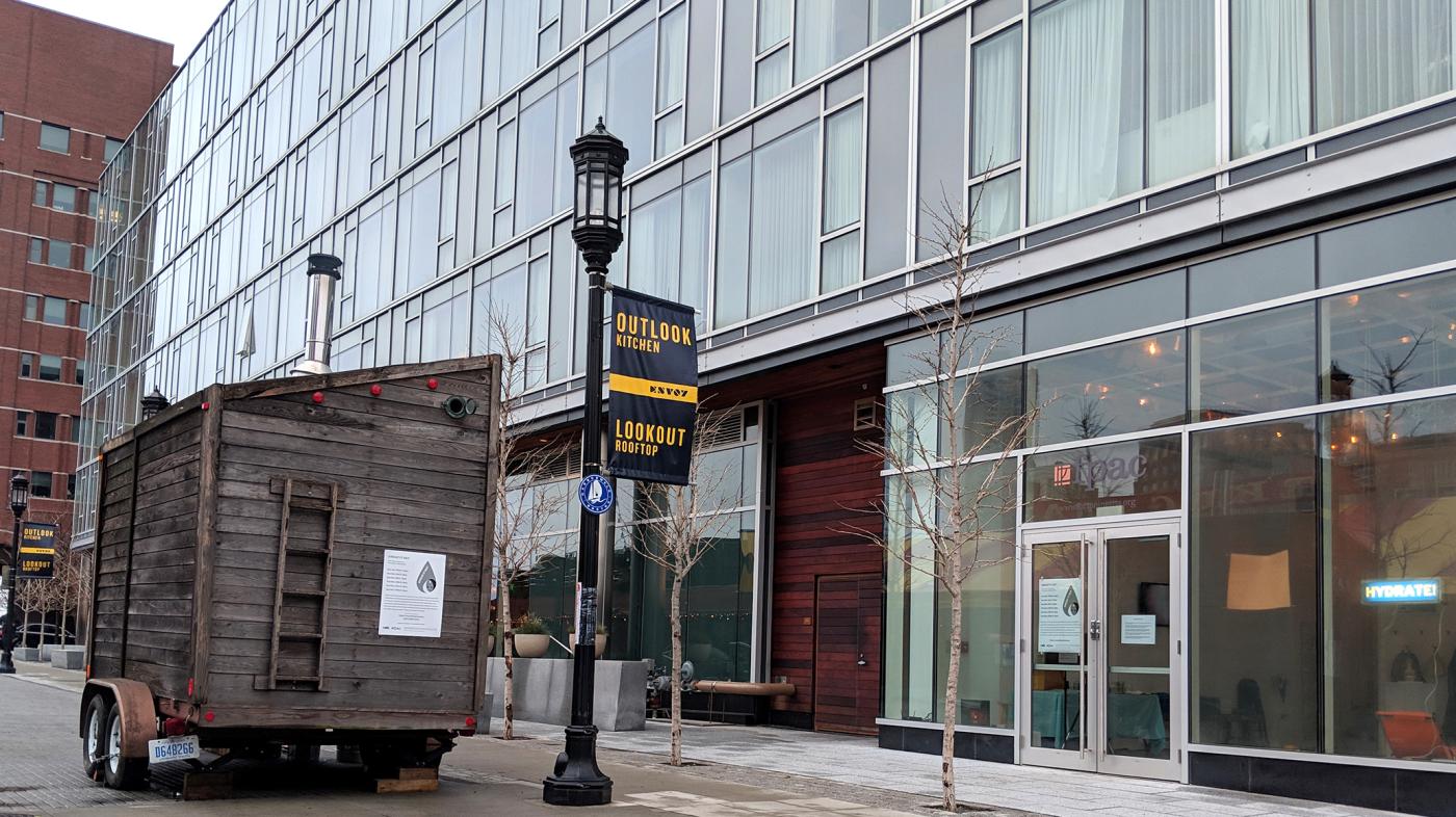 A small wooden lodge, sweatbox, is parked on street next to the Envoy Hotel
