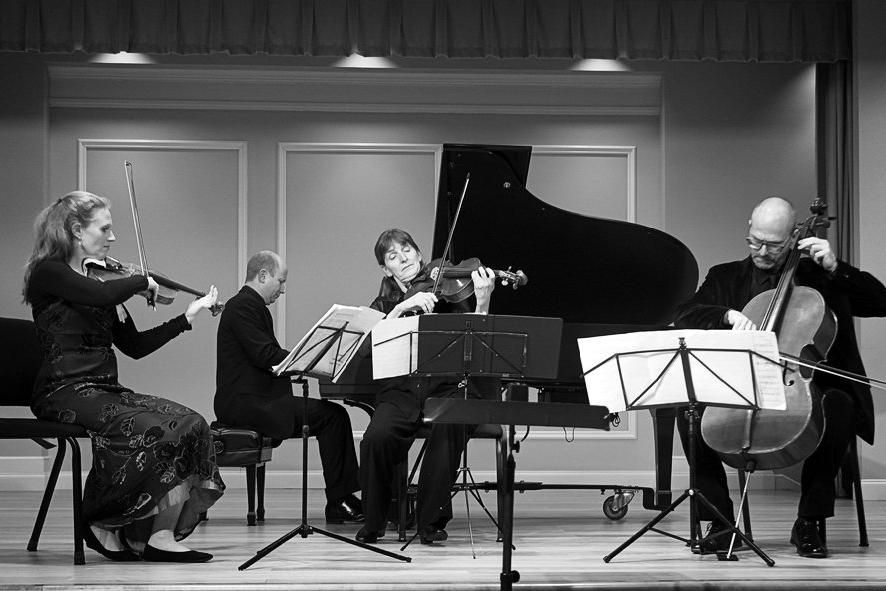 On a stage, a pianist, cellist, and two violinists perform.
